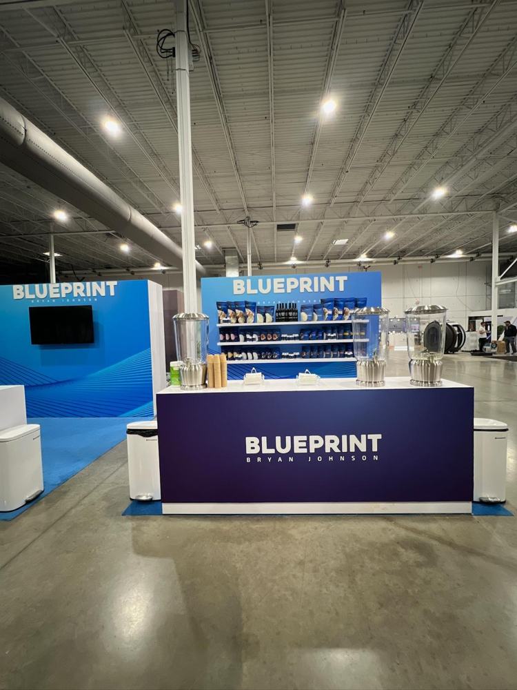 Stand de Blueprint en feria con mostrador de marca y muro de producto